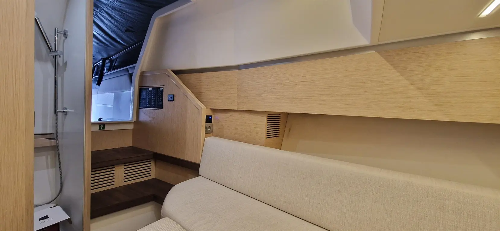 Contemporary boat interior featuring a shower area, a beige sofa, and wooden accents, highlighting space efficiency and comfort.